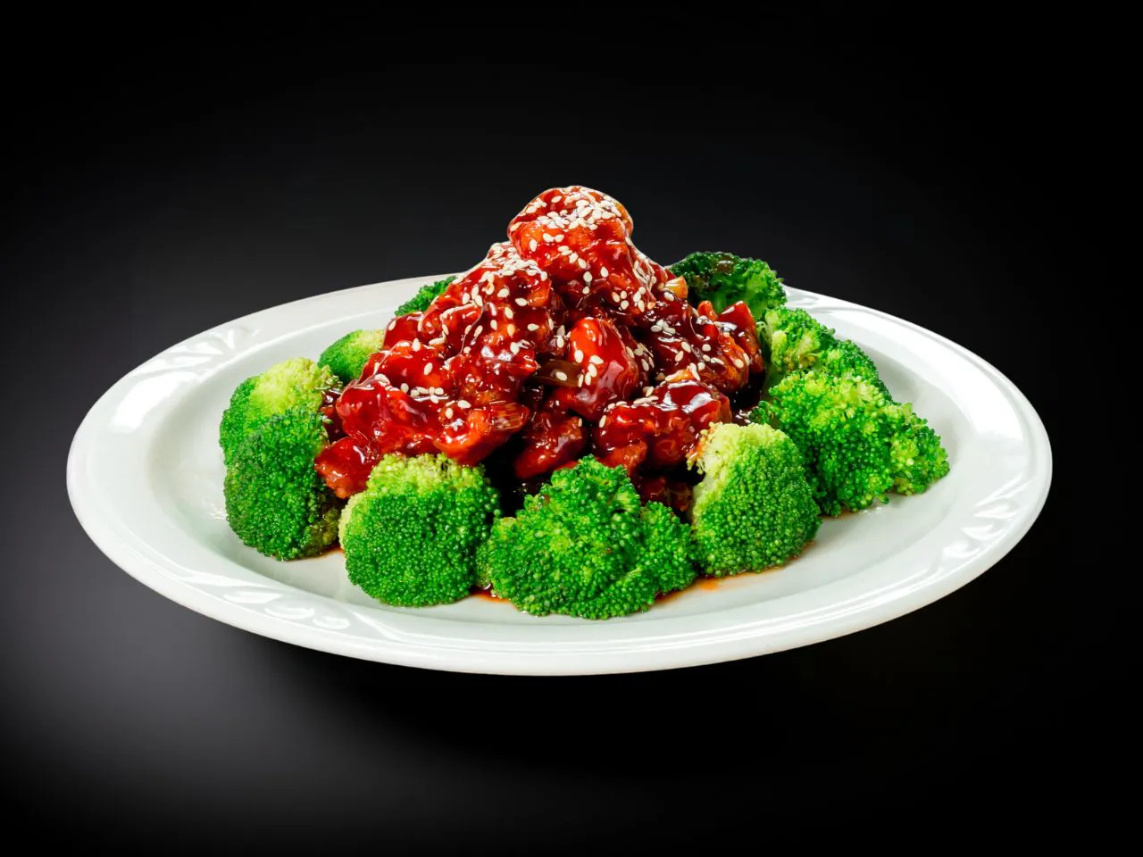 Glossy sesame chicken topped with white sesame seeds and fresh broccoli