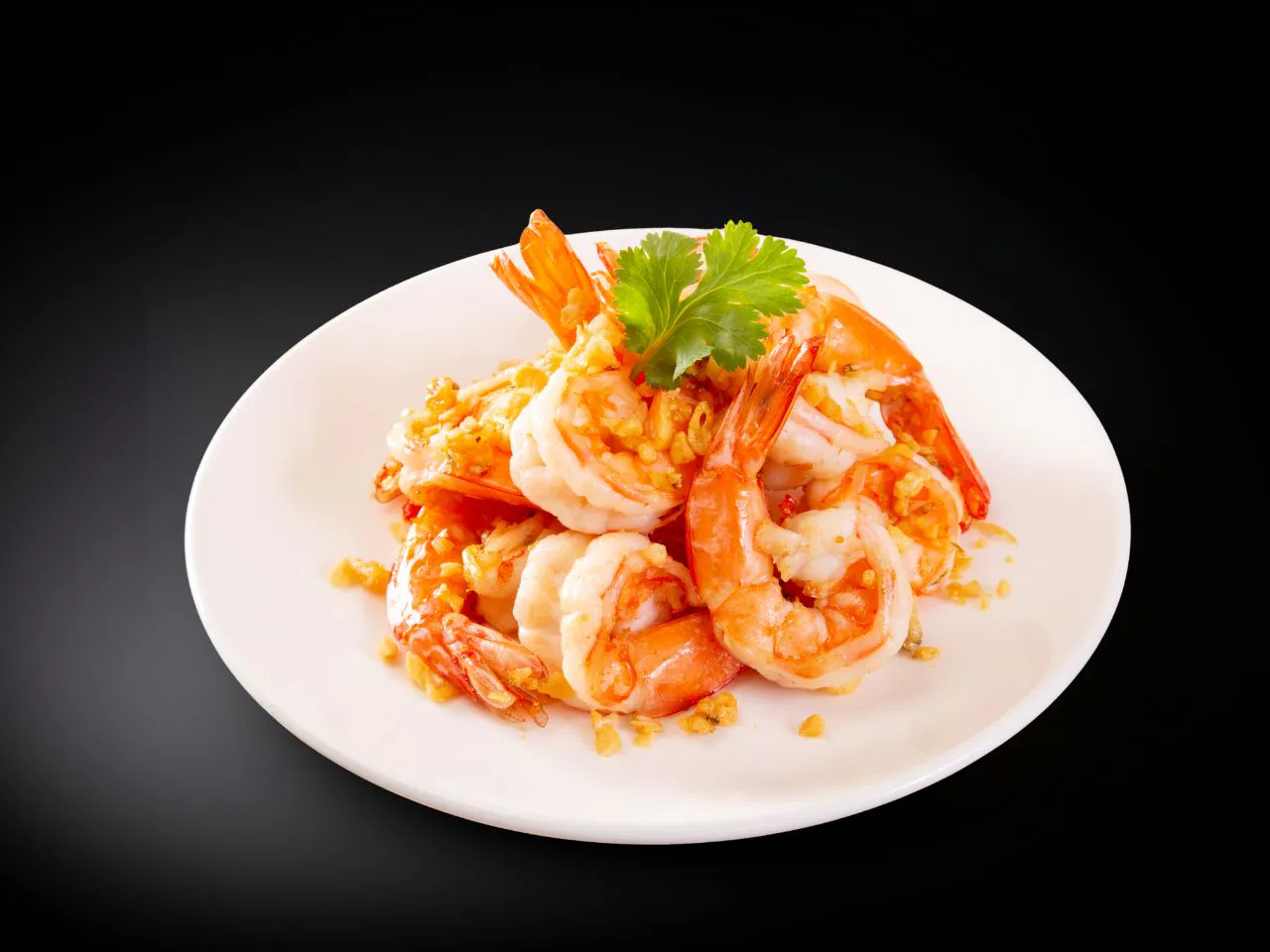 Garlic fried shrimp garnished with fresh cilantro leaf on white plate