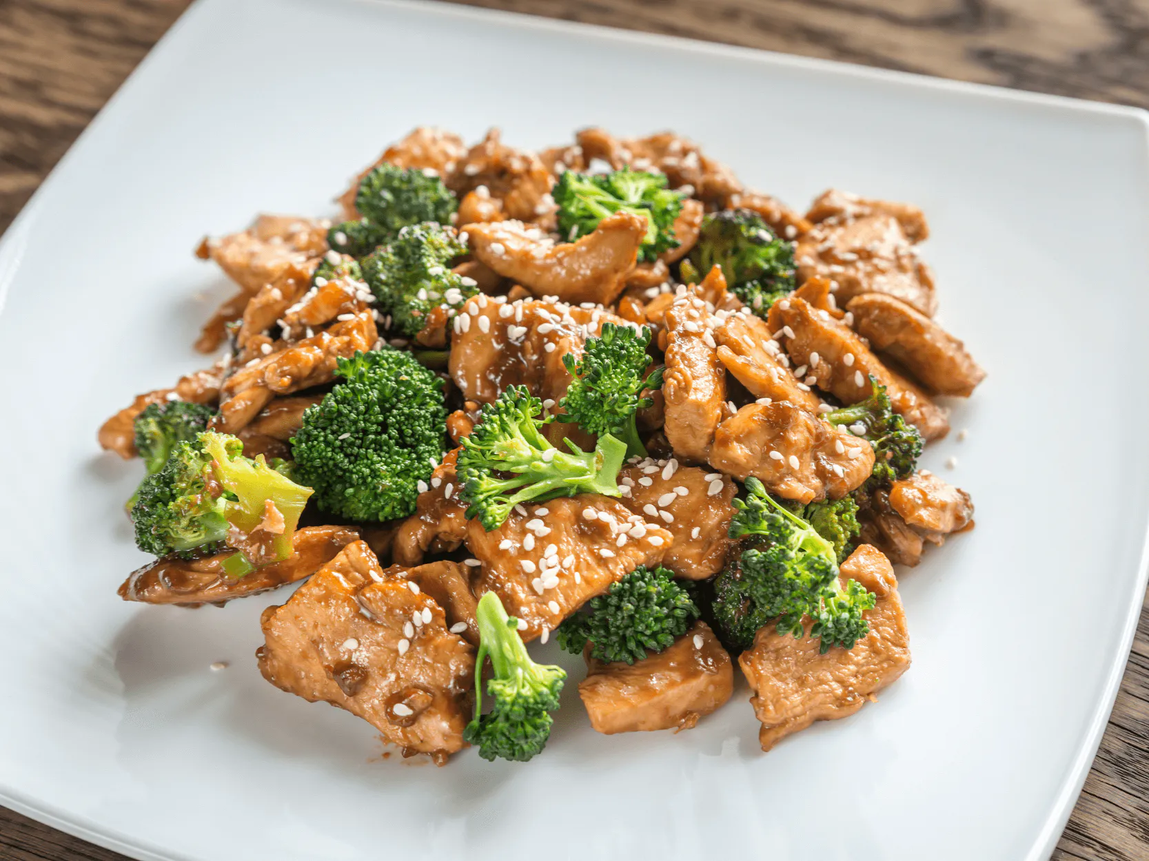 Savory stir‑fried chicken with broccoli and sesame seeds on white square plate